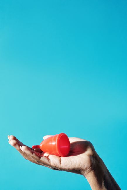 A human hand holding a bright orange, cone-shaped plastic object with a rounded cap, positioned against a clear blue sky background. The hand appears relaxed, with fingers gently supporting the object
