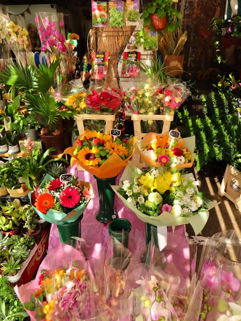 A vibrant display of fresh flower bouquets arranged on a pink table in a flower shop, featuring a variety of colorful flowers including bright yellow sunflowers, pink gerbera daisies, white chrysanthe