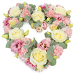 A tender heart-shaped funeral wreath is displayed against a bright white background, its carefully chosen pastel tones offering comfort and calm. The heart is completely filled with flowers, creating a dense, luxurious shape that feels both protective and embracing. Cream and pale yellow roses form the main structure, their velvety petals spiralling outward in soft layers that catch the light subtly, suggesting warmth and purity. Nestled closely alongside them are clusters of pale pink carnations, their pretty, ruffled edges overlapping to add gentle texture and a sense of soft movement, like the hush of voices at a service in one of Bexley's local chapels. Deeper, mauve-pink lisianthus blooms are dotted through the design, their more open, cup-like petals bringing a graceful contrast in both shape and tone, giving the wreath a thoughtful, contemplative depth. Slender stems of eucalyptus thread between the blossoms, the rounded, silvery-green leaves creating a cool, calming backdrop and clearly tracing the curve and point of the heart. Tiny yellowish-green buds are visible here and there, signs of fresh life that sit quietly among the more mature blooms. The composition is balanced and harmonious, with no empty spaces, so the heart appears completely full, a visual echo of love and memories held close. This floral tribute is an eloquent choice for funerals or memorial services across Bexley, offering a gentle way to express sympathy, remembrance, and enduring affection when words are difficult to find.