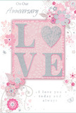 This anniversary card is depicted as a soft celebration of long-lasting love, blending artistic detail with a tenderness that feels very at home in Bexley's quiet residential streets. The centre of the card features the word LOVE in prominent, raised letters, their surfaces brushed with fine glitter that shifts between pearly white, blush pink, and a hint of silver, reminiscent of evening light glinting off petals in a garden along the River Cray. Each letter looks slightly embossed, offering a pleasing contrast between smooth card and sparkling texture. Around this central word, a constellation of delicately illustrated flowers, buds, and swirling leaves spreads across a muted pink background, arranged with the care of a florist shaping an anniversary bouquet. The floral artwork is light and airy: petals traced in slim lines, shaded in soft pastels of blush, ivory, and gentle grey, with scattered silver accents that capture a subtle shimmer without appearing flashy. The flowers and vines curve naturally, giving the impression of movement, as though they are gently opening and unfurling across the card. Interwoven with the floral design, an elegant script spells out a heartfelt anniversary message, the lettering slender and graceful, echoing the card's refined mood. The entire composition feels harmonious and calm, like a treasured keepsake resting on a mantelpiece in a Bexley family home. It conveys the quiet joy, trust, and shared history of a couple marking another year together, its romantic design mirroring the care and consideration that go into choosing the perfect anniversary arrangement for someone deeply loved.